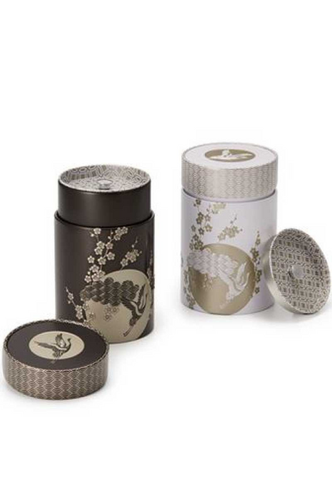 Set de 2 boîtes à thé Komorebi 150g en fer-blanc avec design japonais raffiné. Motifs embossés représentant des grues en vol et des fleurs de cerisier, symboles de longévité et de sérénité. Double fermeture hermétique pour une conservation optimale du thé et des infusions. Disponible en noir et blanc avec finitions dorées.