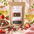 Sachet du thé vert Soleil d'Orient Papothé aux notes de litchi, avec une coupelle de thé en vrac aux morceaux de fraise et de pomme, camomille romaine et pétales de rose, des fraises, une théière et un verre de thé vert