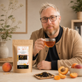 Homme dégustant une tasse de Thé Noir Pêche Abricot Douceurs du Verger Papothé avec sachet kraft, fruits du verger et thé en vrac.